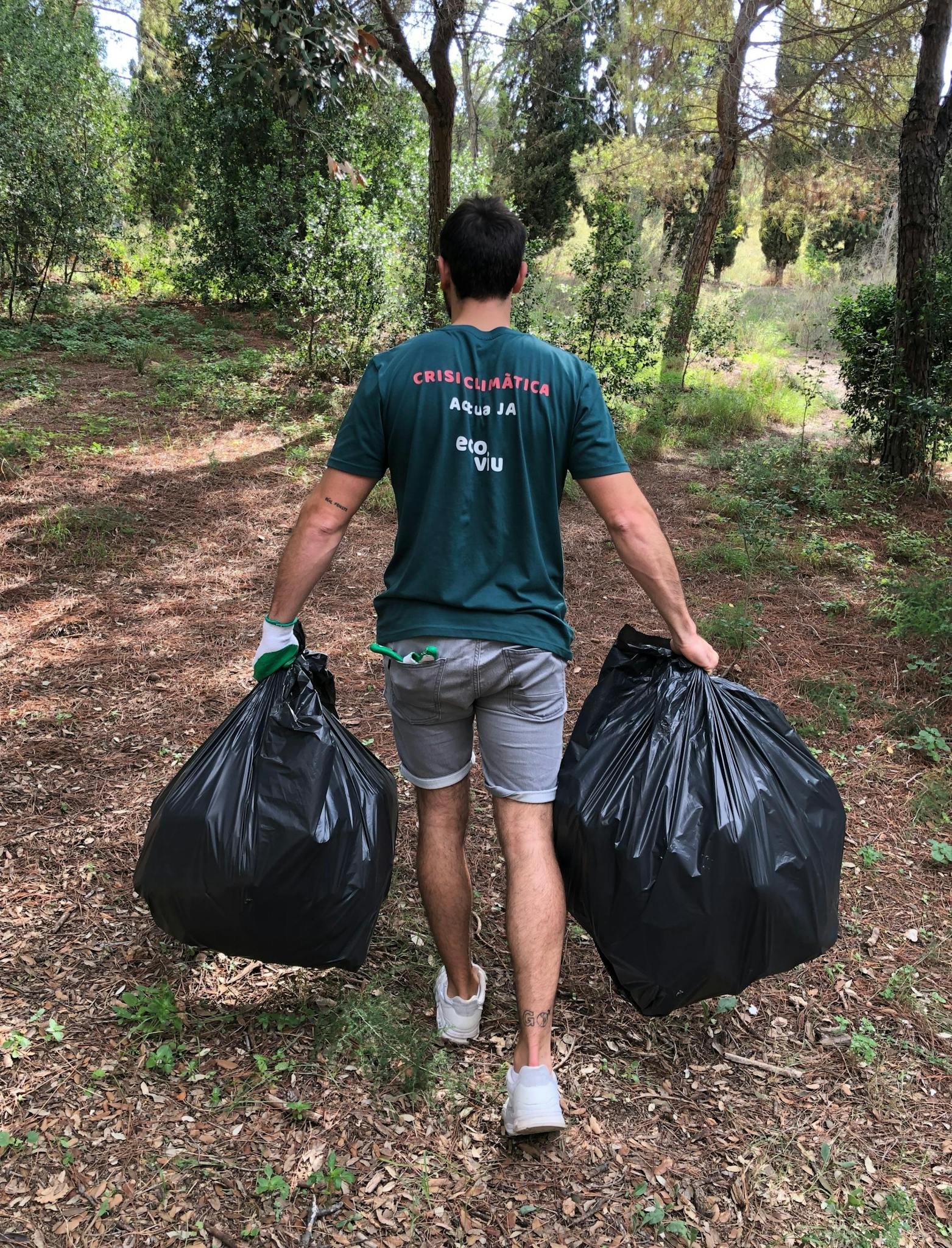 A volunteer cleans up litter in a Barcelona forest, promoting environmental awareness.