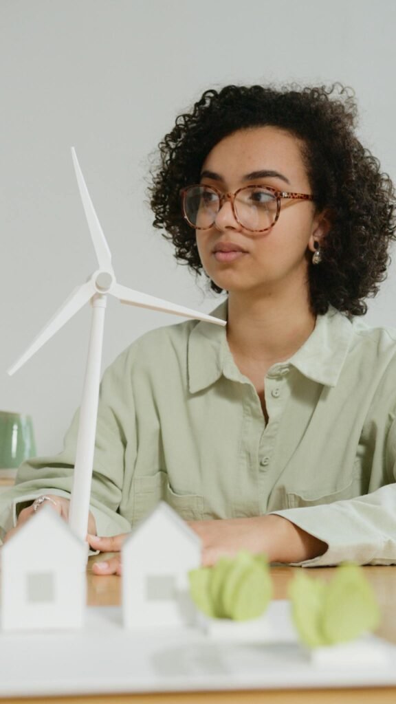 Focused young woman with curly hair looking at a model wind turbine on a desk, symbolizing education and sustainability.